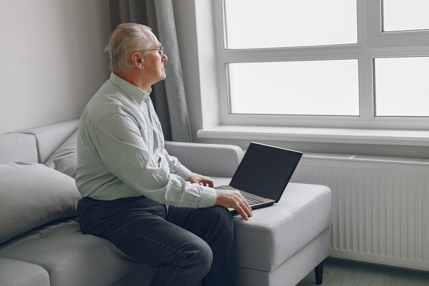 Eleganter alter Mann, der zu Hause sitzt und einen Laptop benutzt