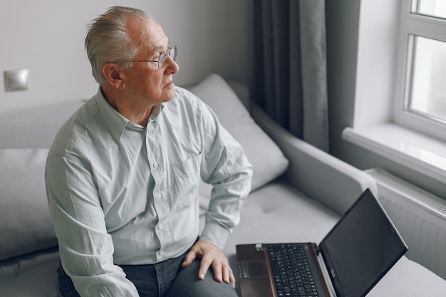 Eleganter alter Mann, der zu Hause sitzt und einen Laptop benutzt