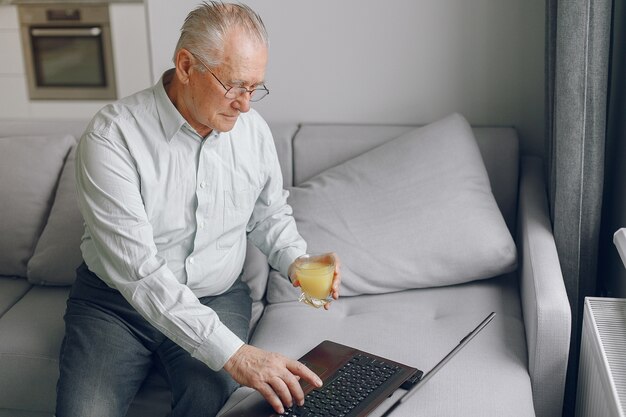 Eleganter alter Mann, der zu Hause sitzt und einen Laptop benutzt