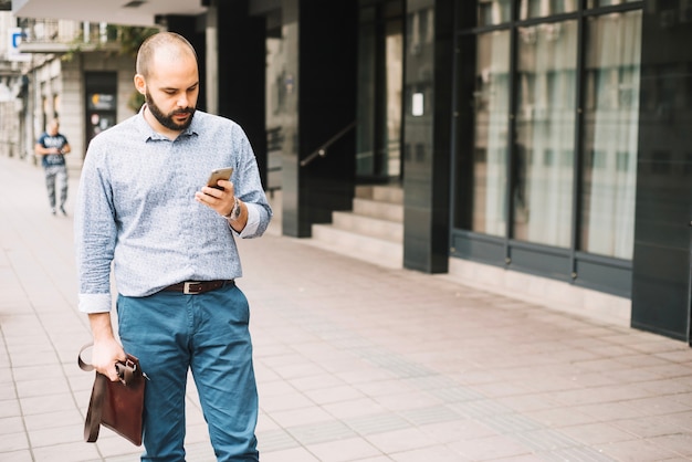 Eleganter Mann, der hinunter Straße mit Smartphone geht