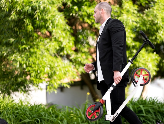 Eleganter Mann, der Roller im Freien trägt