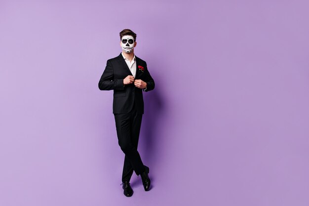 Eleganter Mann, der schwarze klassische Jacke zuknöpft und im entspannten Studio in Maske für Maskerade aufwirft.