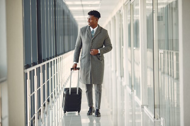 Eleganter schwarzer Mann am Flughafen mit einem Koffer