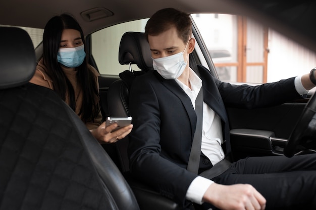 Eleganter Taxifahrer und Kunde in einem Auto mit medizinischen Masken