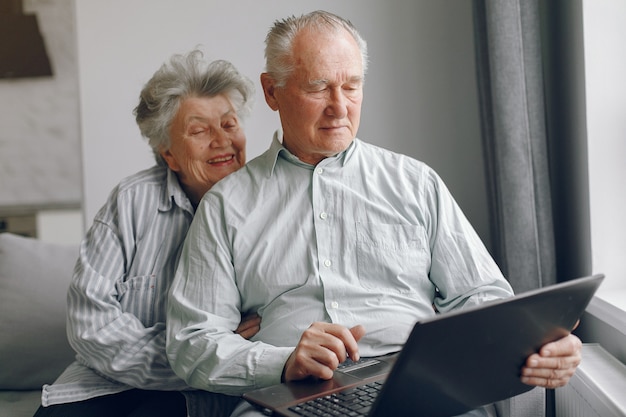 Elegantes altes Ehepaar, das zu Hause sitzt und einen Laptop benutzt