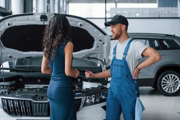 Elegantes Mädchen. Frau im Autosalon mit dem Angestellten in der blauen Uniform, die ihr repariertes Auto zurücknimmt