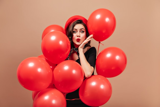 Kostenloses Foto elegantes mädchen in roter baskenmütze und schwarzem kleid bläst kuss und hält riesige luftballons.