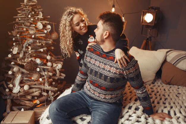 Elegantes Paar, das zu Hause nahe Weihnachtsbaum sitzt