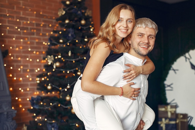 Elegantes Paar, das zu Hause nahe Weihnachtsbaum steht