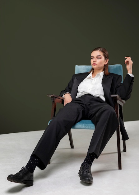 Elegantes weibliches Modell, das in einem Sessel in einem Jackenanzug sitzt. neues Weiblichkeitskonzept