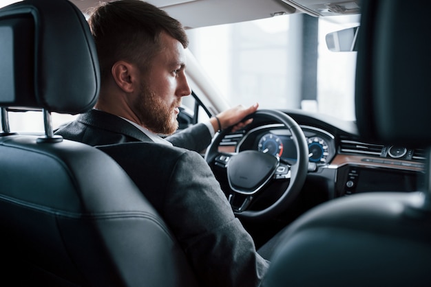 Eleganz und Schönheit. Moderner Geschäftsmann, der sein neues Auto im Autosalon versucht