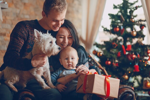 Eltern, die mit einem Hund und einem Baby mit einem Hintergrund Weihnachtsbaum
