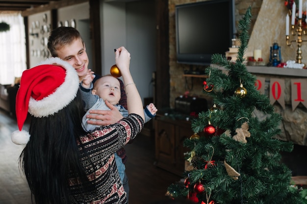 Kostenloses Foto eltern ihr kind eine weihnachtskugel zeigt