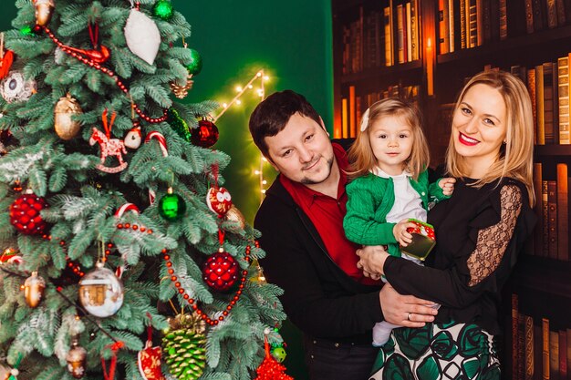 Eltern mit wenigem blondem Mädchen werfen vor einem Weihnachtsbaum im Raum auf