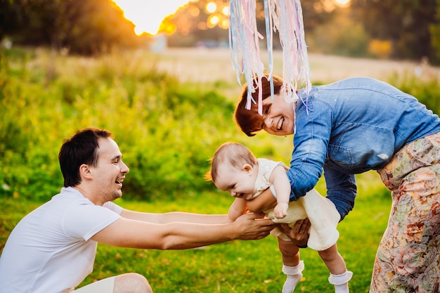 Kostenloses Foto eltern spielen mit ihrem kleinen mädchen unter den bändern, die vom baum hängen