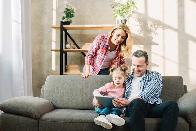 Eltern und Tochter, die zu Hause digitale Tablette auf Sofa im Wohnzimmer verwendet