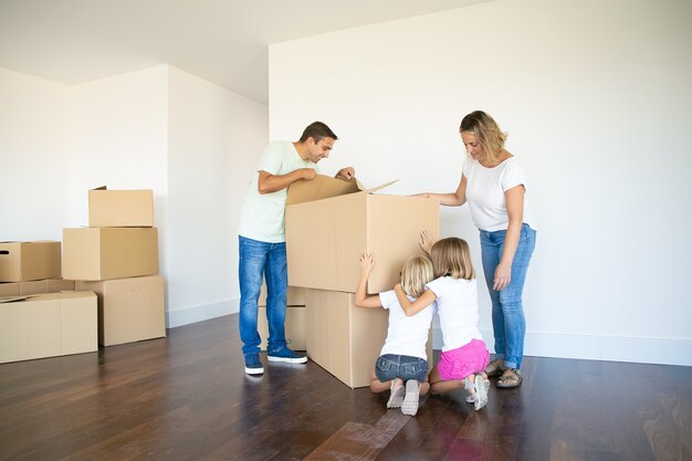 Eltern und zwei Töchter haben Spaß beim Öffnen von Kisten und Auspacken in ihrer neuen leeren Wohnung