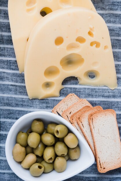 Emmentaler Käsescheiben; Brot und frische Oliven auf Tischdecke