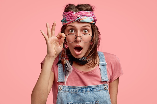 Kostenloses Foto emotional überraschte junge hippie-frau hält hand am rand der runden brille