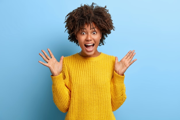 emotionale Frau mit einem Afro, der in einem rosa Pullover aufwirft