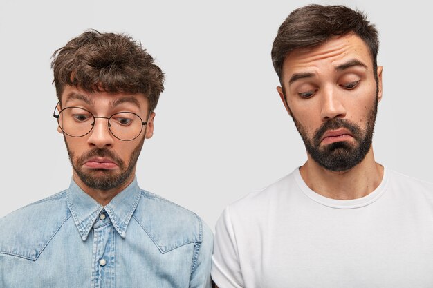 Emotionale Zwei-Mann-Kollegen konzentrierten sich mit überraschten Gesichtsausdrücken, lässig gekleidet, haben dicke dunkle Bärte und bemerken etwas Erstaunliches