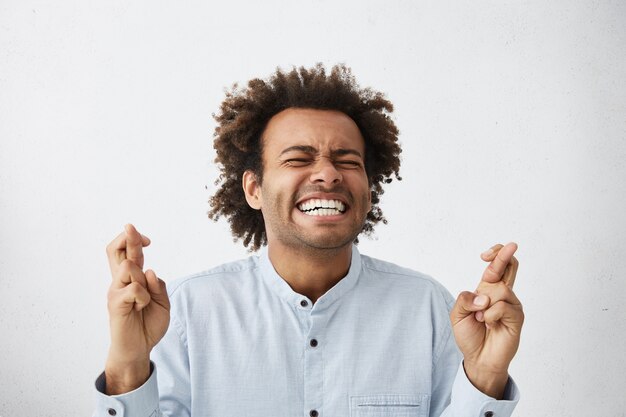 emotionaler junger männlicher Bewerber, der die Augen fest schließt und die Finger kreuzt