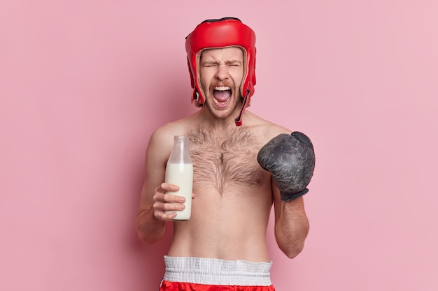 Emotionaler männlicher Boxer ruft laut aus und hält den Mund offen, trinkt Milch für starke Muskeln
