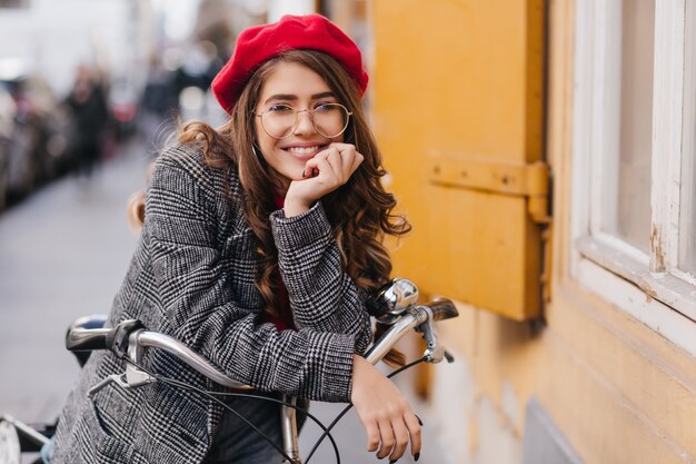 Emotionales süßes Mädchen mit verträumter lockiger Frisur, die auf Fahrrad aufwirft