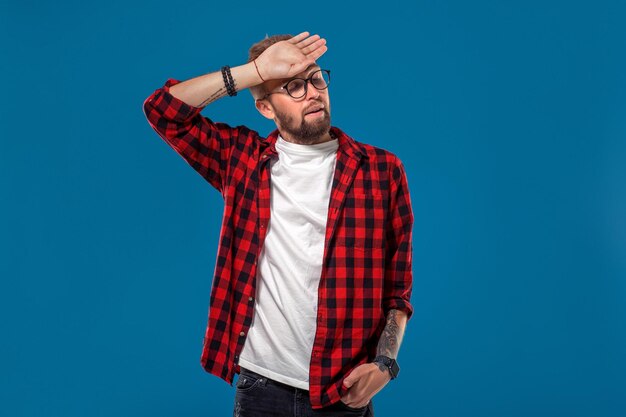 Emotionales und menschliches Konzept: junger bärtiger Mann im karierten Hemd. Hipster-Stil. Studioaufnahme auf blauem Hintergrund. Platz kopieren