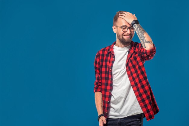 Emotions- und Personenkonzept: junger bärtiger Mann im karierten Hemd. Hipster-Stil. Studioaufnahme auf blauem Hintergrund. Platz kopieren