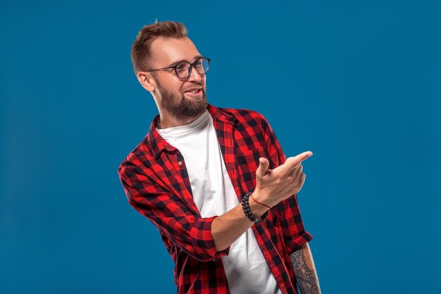 Emotions- und Personenkonzept: junger bärtiger Mann im karierten Hemd. Hipster-Stil. Studioaufnahme auf blauem Hintergrund. Platz kopieren