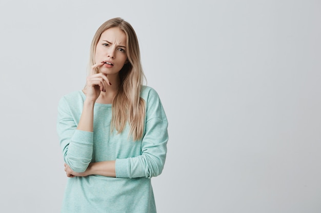 Empörte blonde Frau, die mit den Ergebnissen der Prüfung oder des Wettbewerbs unzufrieden ist. hält den Finger auf dem geöffneten Mund