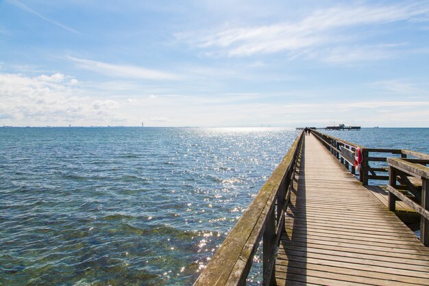 Endlos aussehender Holzsteg an der Nordsee unter blauem Wolkenhimmel