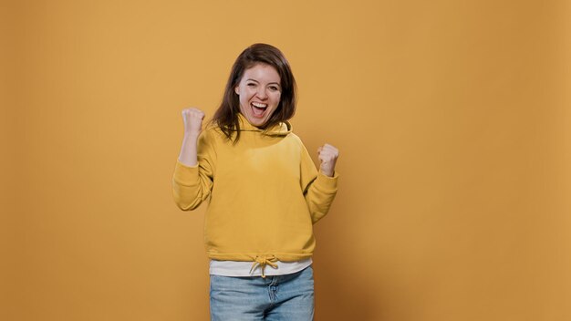 Energetische und ekstatische Frau, die den Erfolg genießt und mit der Handgeste ja den Sieg im Studio feiert. Selbstbewusste, lässige Person, die fröhlich lächelt und sich wie ein Gewinner fühlt, der glücklich ist.