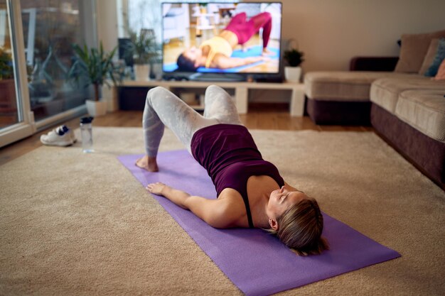 Engagierte Athletin, die ihre Hüften anhebt und während des Heimtrainings Glute Bridge-Übungen macht