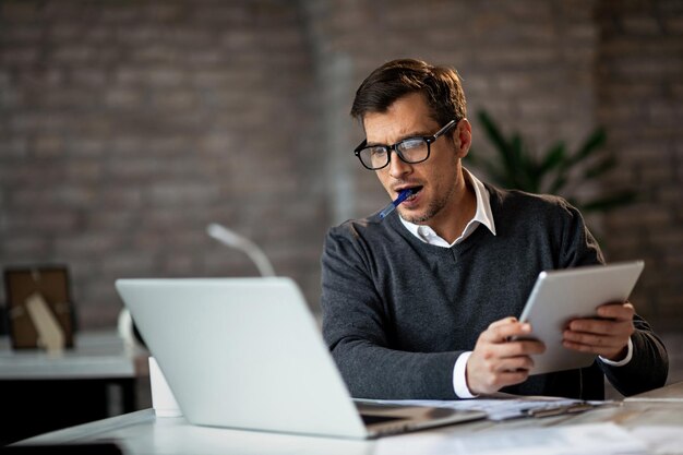 Engagierter Geschäftsmann mit Laptop und digitalem Tablet während der Arbeit im Büro
