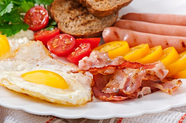 Englisches Frühstück - Spiegeleier, Speck, Würstchen und geröstetes Roggenbrot