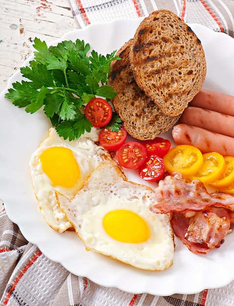 Kostenloses Foto englisches frühstück - spiegeleier, speck, würstchen und geröstetes roggenbrot