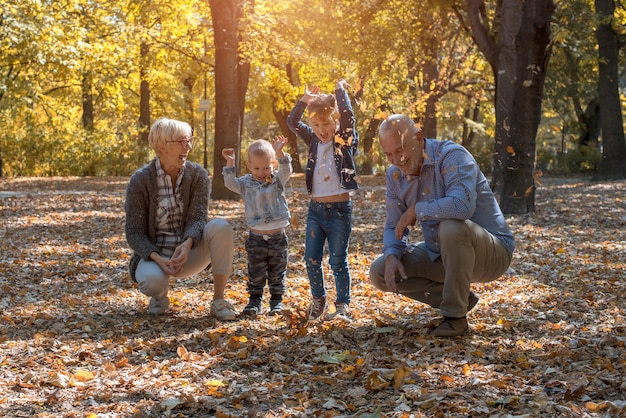 Enkel und Großeltern werfen Blätter im Park und verbringen Zeit miteinander