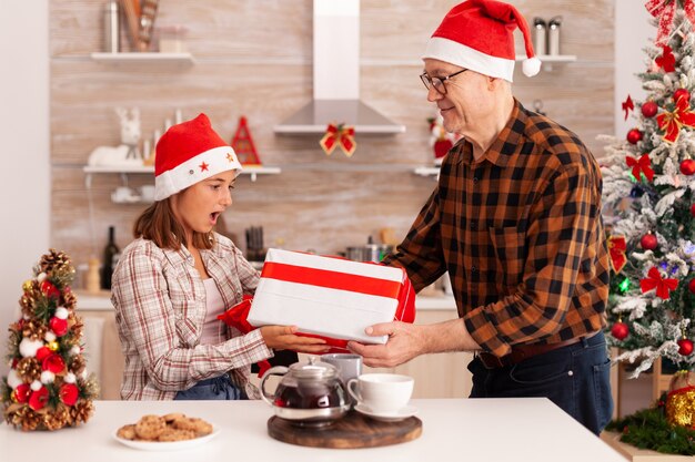 Enkelin überrascht Großvater mit Verpackungsgeschenk, das Weihnachtsfeiertage feiert