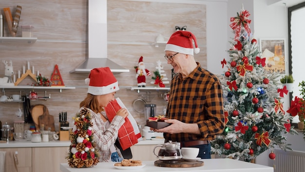 Enkelkind mit Großvater, der mit Weihnachtspapier ein Geschenk mit Schleife darauf bringt