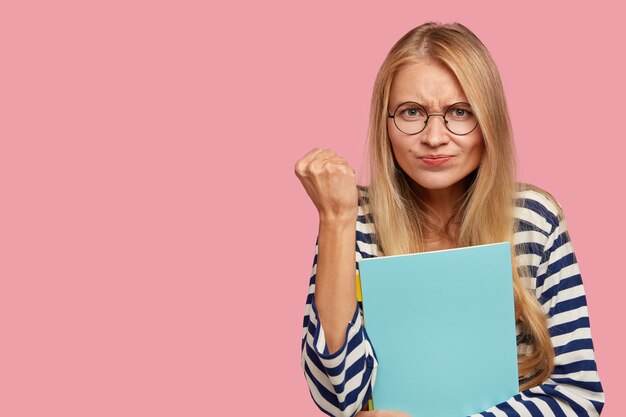 entschlossener blonder Student, der gegen die rosa Wand aufwirft