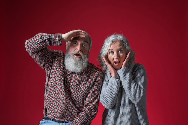 Entsetzte ältere Paare, die zur Kamera gegen roten Hintergrund schauen