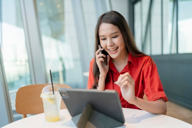 Entspannen Sie sich in der Freizeit attraktive, intelligente asiatische freiberufliche Unternehmerinnen lächeln und genießen Sie die Arbeit mit Smartphone und Laptop im Café mit unscharfem City-Business-Konzept für digitale Nomaden-Casual-Ideen