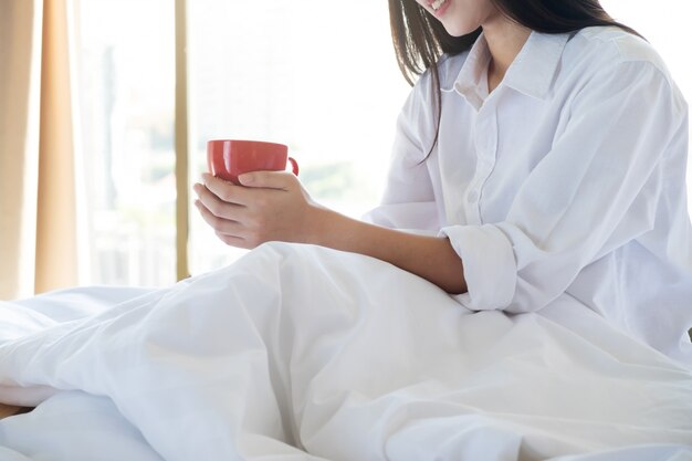 Entspannende junge Frau, die ihren Kaffee beim Sitzen im Bett genießt.