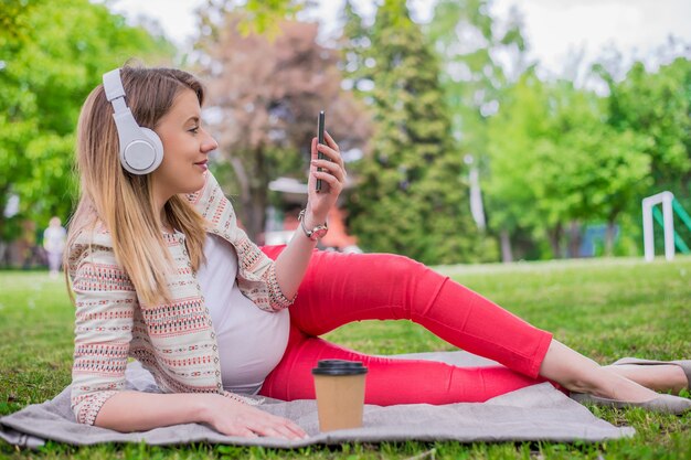 Entspannte Frau hört die Musik mit Kopfhörern auf dem Gras liegen. Schöne junge Frau mit Kopfhörer genießt in der Musik beim Liegen in der Natur, Genießen Sie Musik