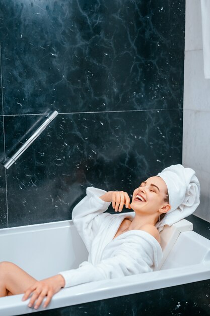 Entspannte Frau mit Handtuch auf Haar in der Badewanne liegend