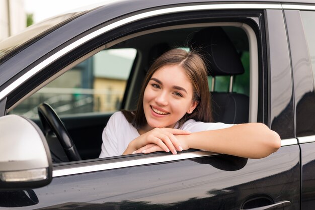 Entspannte glückliche Frau auf Sommer-Roadtrip-Reiseurlaub, der aus Autofenster auf Wand des blauen Himmels lehnt.