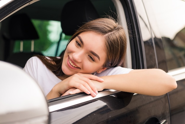 Entspannte glückliche Frau auf Sommer-Roadtrip-Reiseurlaub, der aus Autofenster auf Wand des blauen Himmels lehnt.