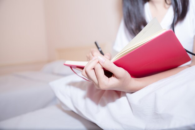 Entspannte junge Frau in den Pyjamas Tagebuch auf ihrem Bett schreibend